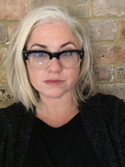 Image of a caucasian woman with blonde hair in a bob and spectacles staring straight at the camera